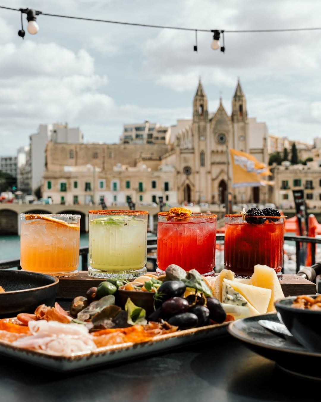 Signature cocktails and a sharing platter on Klay's terrace, facing the neo-gothic Carmelite church across Balluta Bay
