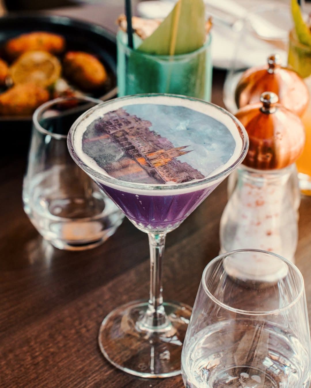 A violet gin cocktail topped with an edible print, on the bar at Klay