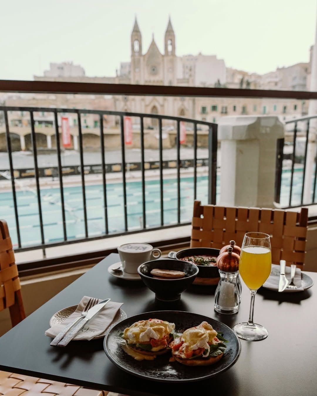 Eggs Benedict and fresh juice at a window table overlooking the Balluta lido and church
