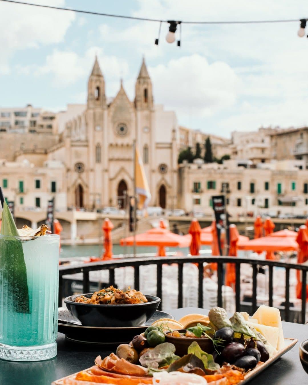 A sharing platter and a cocktail on a terrace table facing the Carmelite church