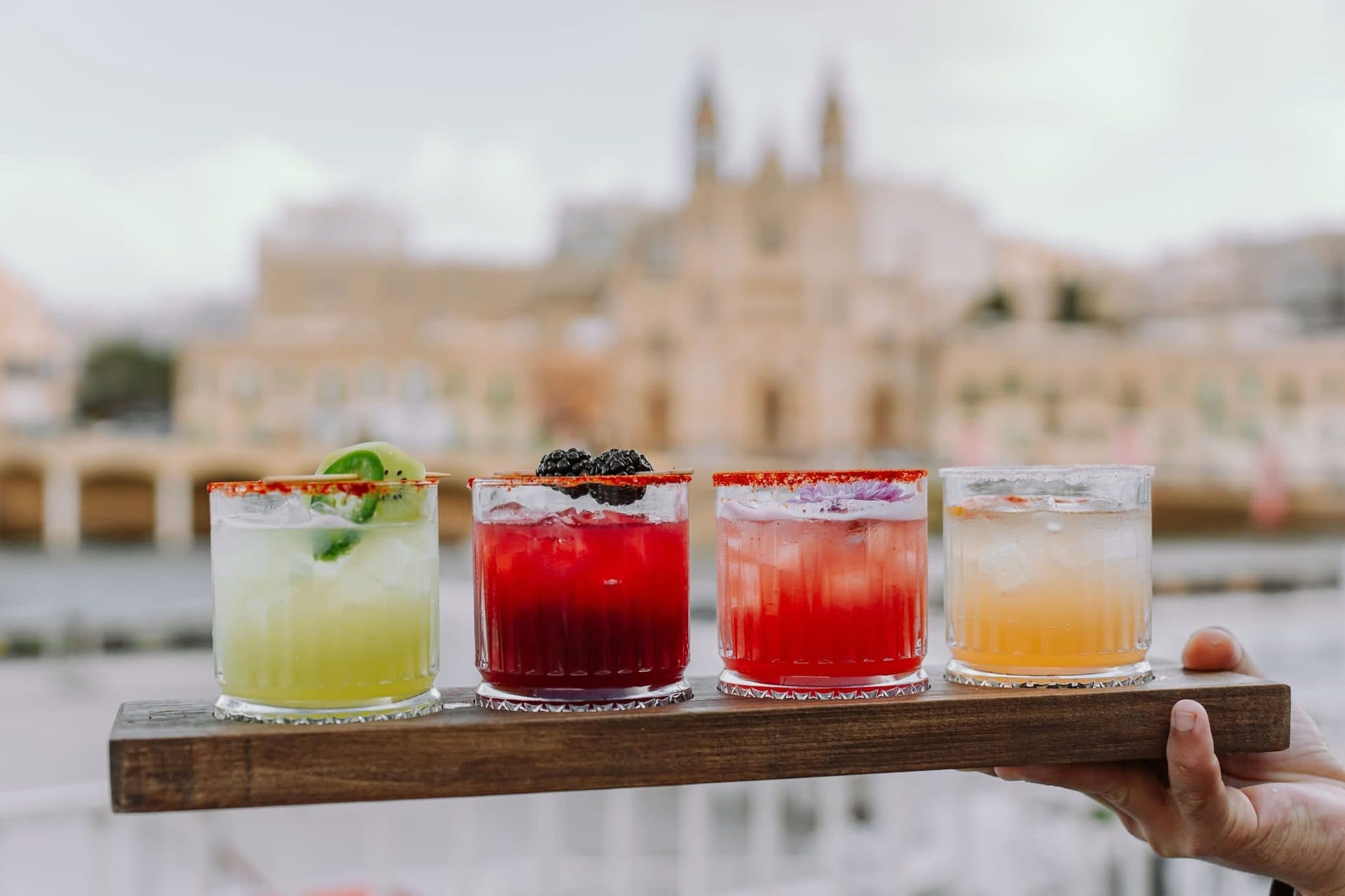 A flight of four house cocktails held up against Balluta Bay and its church